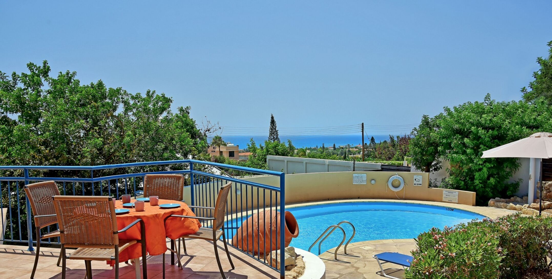 A poolside area with a table and chairs, a lifebuoy, and a view of the sea.