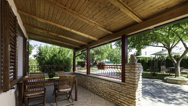 A covered patio with wooden furniture and a stone wall, overlooking a garden with trees and a gazebo. - House / Villa - Rovinj (Rovinj)
