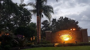 A sign for Bahama Bay Resort with a beach scene illustration, surrounded by lush greenery and palm trees.