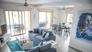 Ein modernes Wohnzimmer mit einem grauen Sofa, einem Flachbildfernseher und einem Essbereich mit Tisch für vier Personen.