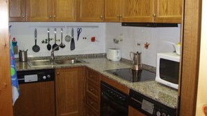 Una cocina con armarios de madera, un lavamanos de acero inoxidable, un lavavajillas, una estufa y un microondas.