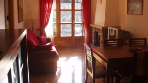 Una sala de estar acogedora con un sofá, una mesa de comedor con sillas, una chimenea y un ventanal con cortinas.