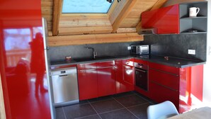 Eine moderne Küche mit roten Schränken, einem Geschirrspüler, einer Spüle und einer Mikrowelle. Über der Spüle befindet sich ein Oberlicht und über der Arbeitsplatte ein kleines Fenster.