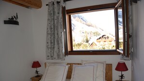 Ein Schlafzimmer mit einem hölzernen Bett, zwei Nachttischen mit Lampen, einem Fenster mit Bergblick und einem dekorativen Wandbild.