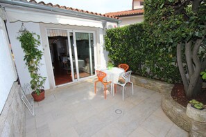 Un patio con tavolo e sedie, una pianta in vaso e una porta scorrevole in vetro che dà su un ambiente interno.