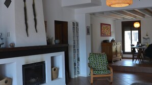 A spacious living room with a fireplace, a wooden coffee table, a patterned armchair, and a dining area with a table and chairs. - The African House, rural getaway between Ronda and Málaga (Tolox)