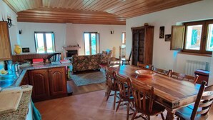 Una cocina amplia con armarios de madera, una mesa de comedor con sillas, una chimenea y ventanas grandes.