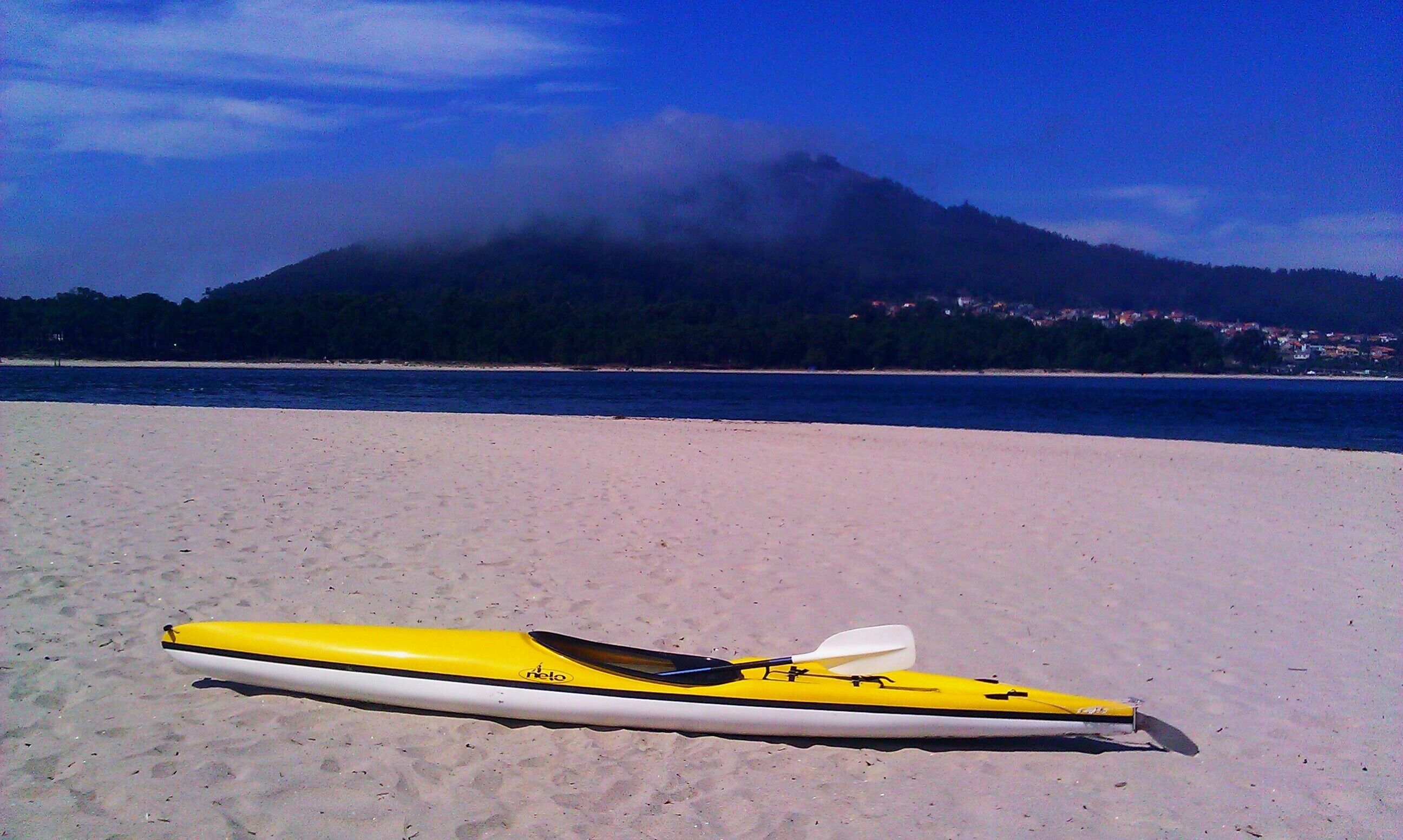 Un kayak sur une plage de sable, avec une montagne et une côte en arrière-plan.