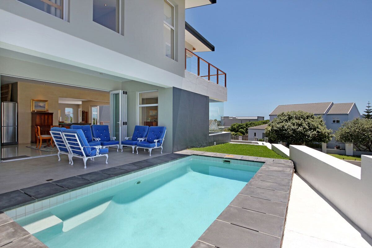A modern house with a swimming pool, blue lounge chairs, and a glass door leading to the interior.