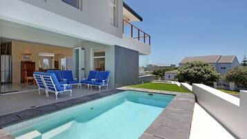 A modern house with a swimming pool, blue lounge chairs, and a glass door leading to the interior.