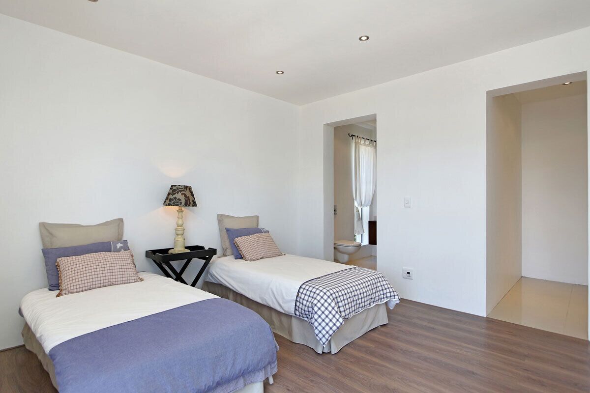 A bedroom with two single beds, a nightstand with a lamp, and a bathroom visible through an open door.