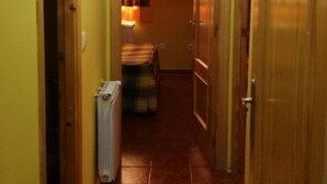 Een smalle gang met gele wanden en een betegelde vloer. Aan beide kanten bevinden zich houten deuren, en in het midden staat een radiator.