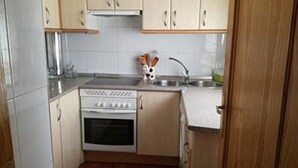 Een kleine keuken met een kookplaat, oven, spoelbak en houten kastjes.
