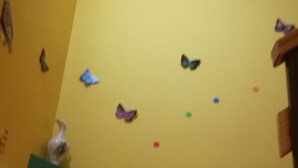 Een kamer met een gele wand, een groen bord met kleurrijke letters en vlinderdecoraties.