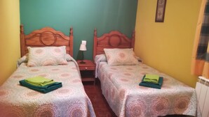 Een kamer met twee eenpersoonsbedden, elk met een bed met decoratieve spreien en kussens, een nachtkastje met een lamp, en een inlijsting foto aan de muur.