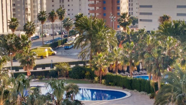 A resort with multiple swimming pools surrounded by palm trees and a cityscape in the background.