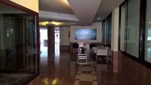 A modern lobby with a glass partition, a seating area with chairs and a table, and a large painting on the wall.
