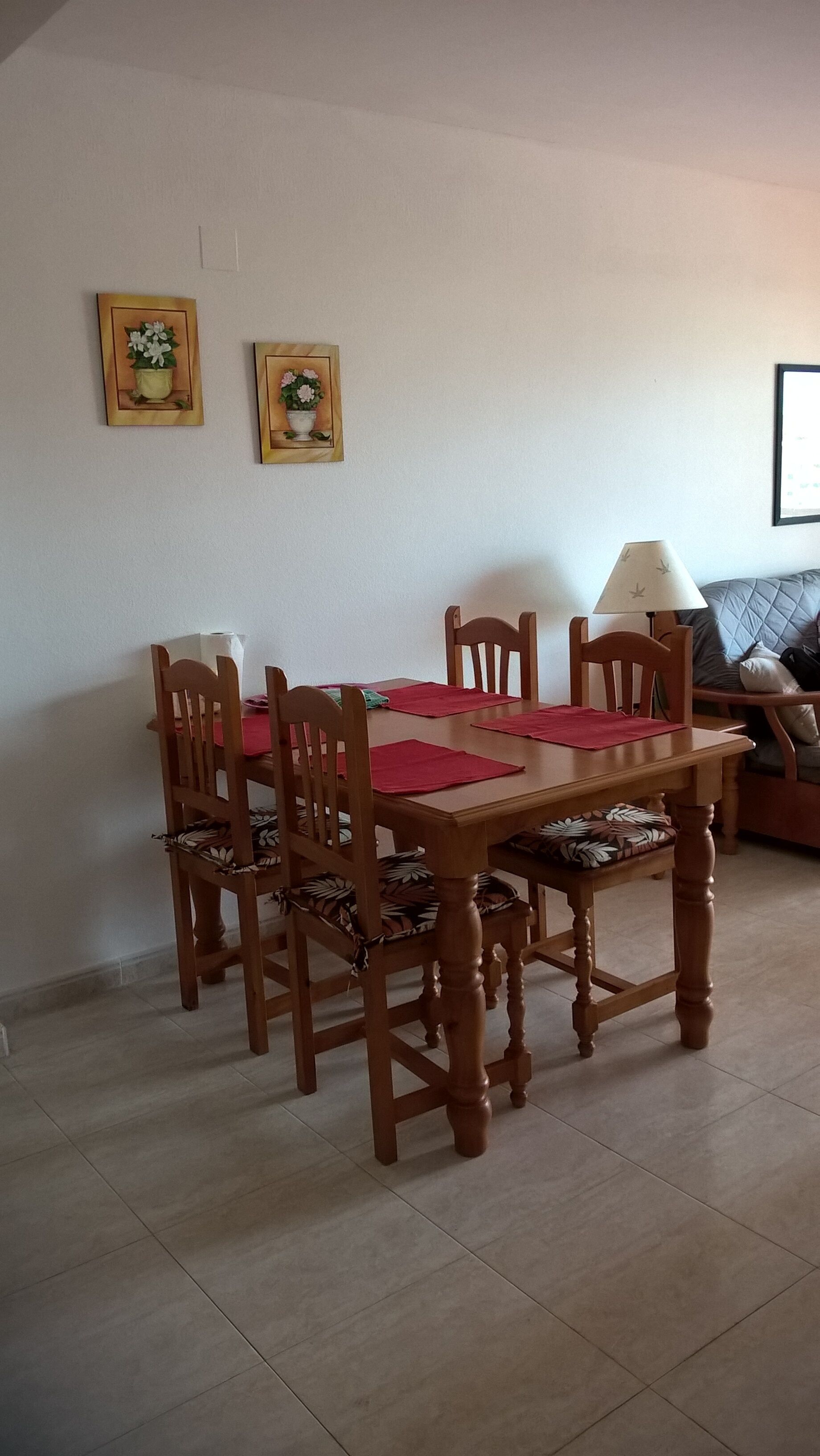 A dining area with a wooden table and chairs, a red placemat, and two framed floral pictures on the wall.