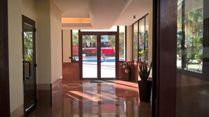 A hotel lobby with a checkered floor, large windows, and a view of a swimming pool and palm trees outside.