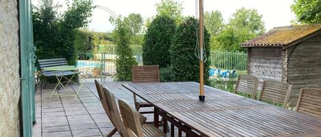 Een terras buiten met een houten tafel en stoelen, een grote parasol en een stenen muur.