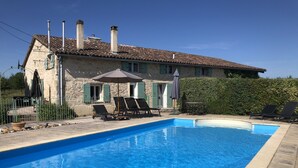 A swimming pool with lounge chairs and umbrellas, a stone building with chimneys, and a hedge. - Charming farmhouse with private pool in secluded location.  (Monteton)