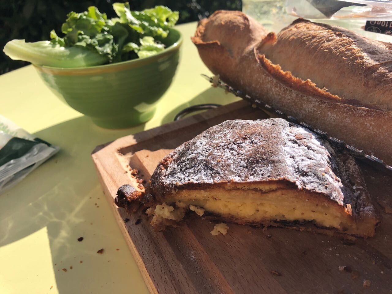 Ein Stück Schichttorte auf einer Holzbrett, ein Brotlaib und eine grüne Schüssel mit Salaten.