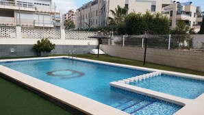 A rectangular swimming pool with a clear blue water surface, surrounded by a white tiled deck and a low green artificial turf area. - Beautiful duplex apartment with pool 200 meters from the beach and golf (el campello muchavista)