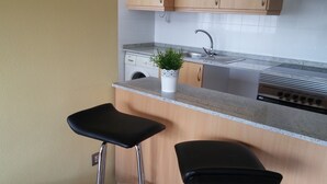 A kitchen with a granite countertop, stainless steel sink, and a built-in oven. There are two black bar stools and a potted plant on the counter. - Beautiful duplex apartment with pool 200 meters from the beach and golf (el campello muchavista)
