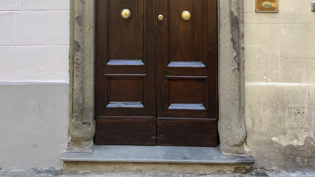 A double wooden door with a stone arch and a shield emblem above it.