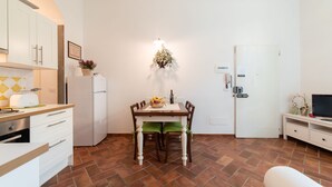 A compact kitchen with white cabinets, a built-in oven, a refrigerator, and a dining table with chairs.