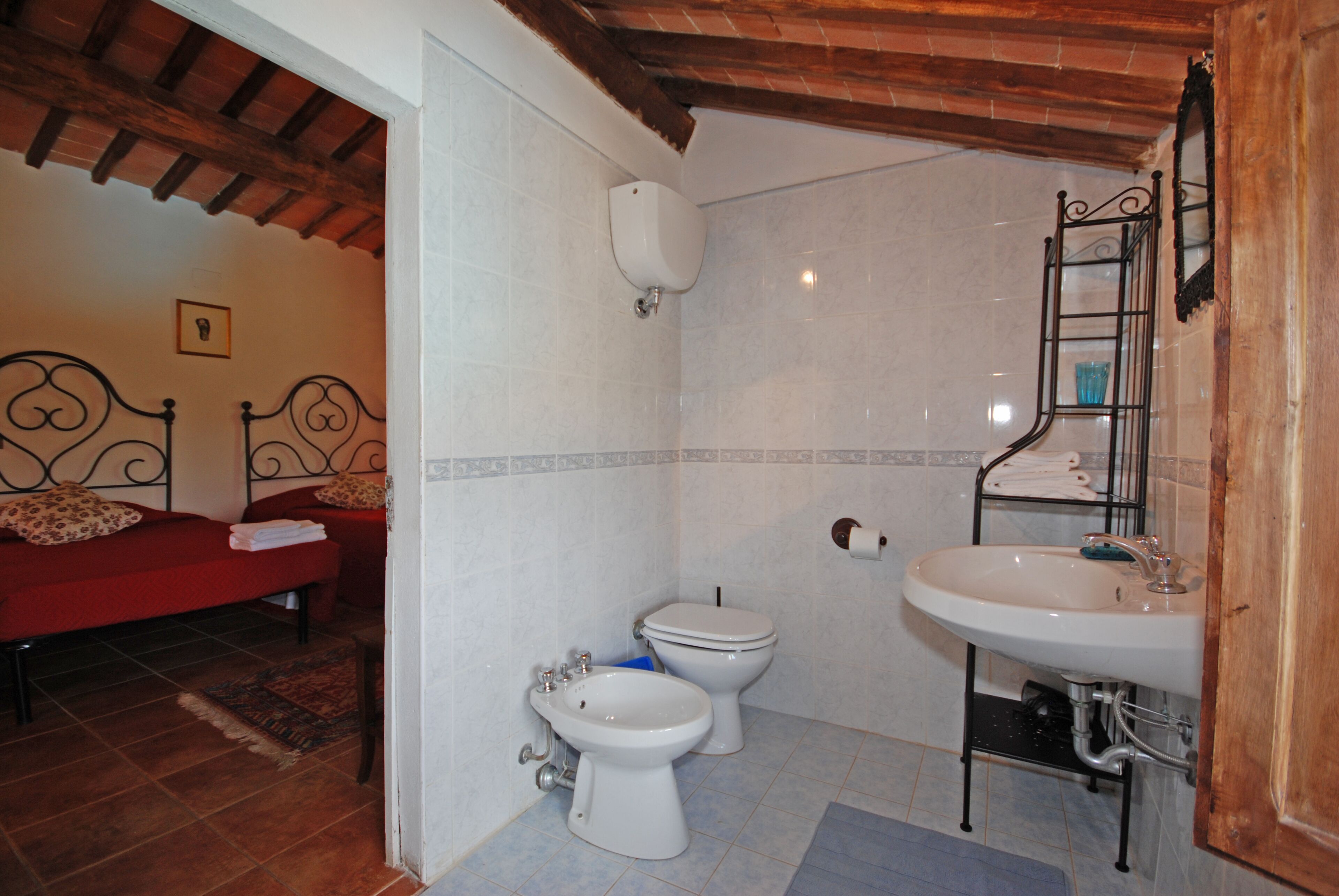Une salle de bain avec des toilettes, un bidet, un lavabo et un lit recouvert d’une couverture rouge.