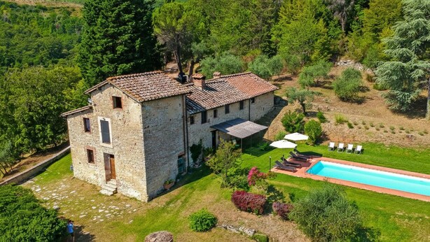 A stone building with a tiled roof, a swimming pool, and a garden with various plants and trees.