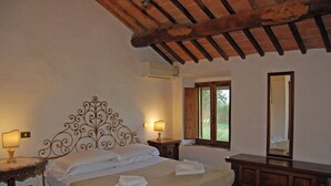 Un dormitorio con una cama grande, cabecera de madera, mesitas de noche con lámparas, un espejo y una ventana con vistas al verdor.