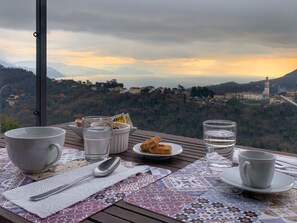A table set with a cup, a glass of water, a plate with cookies, and a spoon, overlooking a scenic view of a town with mountains and a church.
