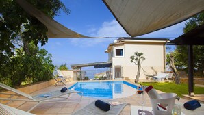 Uma área à beira da piscina com espreguiçadeiras, piscina e um pequeno edifício ao fundo.