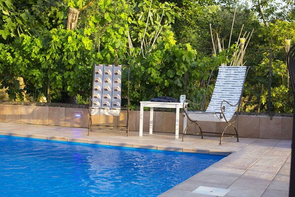 A poolside area with a pool, two chairs, a table, and a patterned towel.