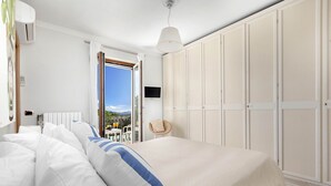 Quarto com uma cama grande, guarda-roupa, televisão e varanda com vista.