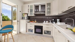 Cozinha moderna com armários brancos, forno embutido, micro-ondas e máquina de café.