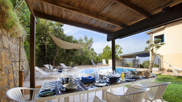 Uma área de refeições ao ar livre com piscina, assentos cobertos e vista para a paisagem circundante.