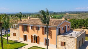 A two-story house with a stone facade, multiple windows with shutters, and a balcony with sun loungers.