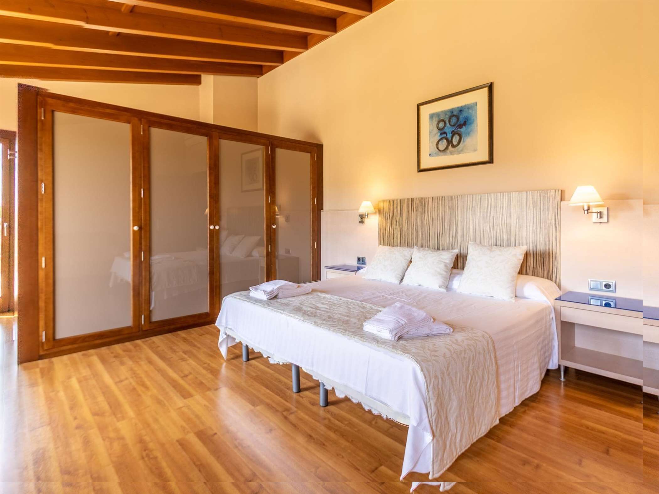 A bedroom with a large bed, wooden flooring, a sliding glass door, and a framed picture on the wall.