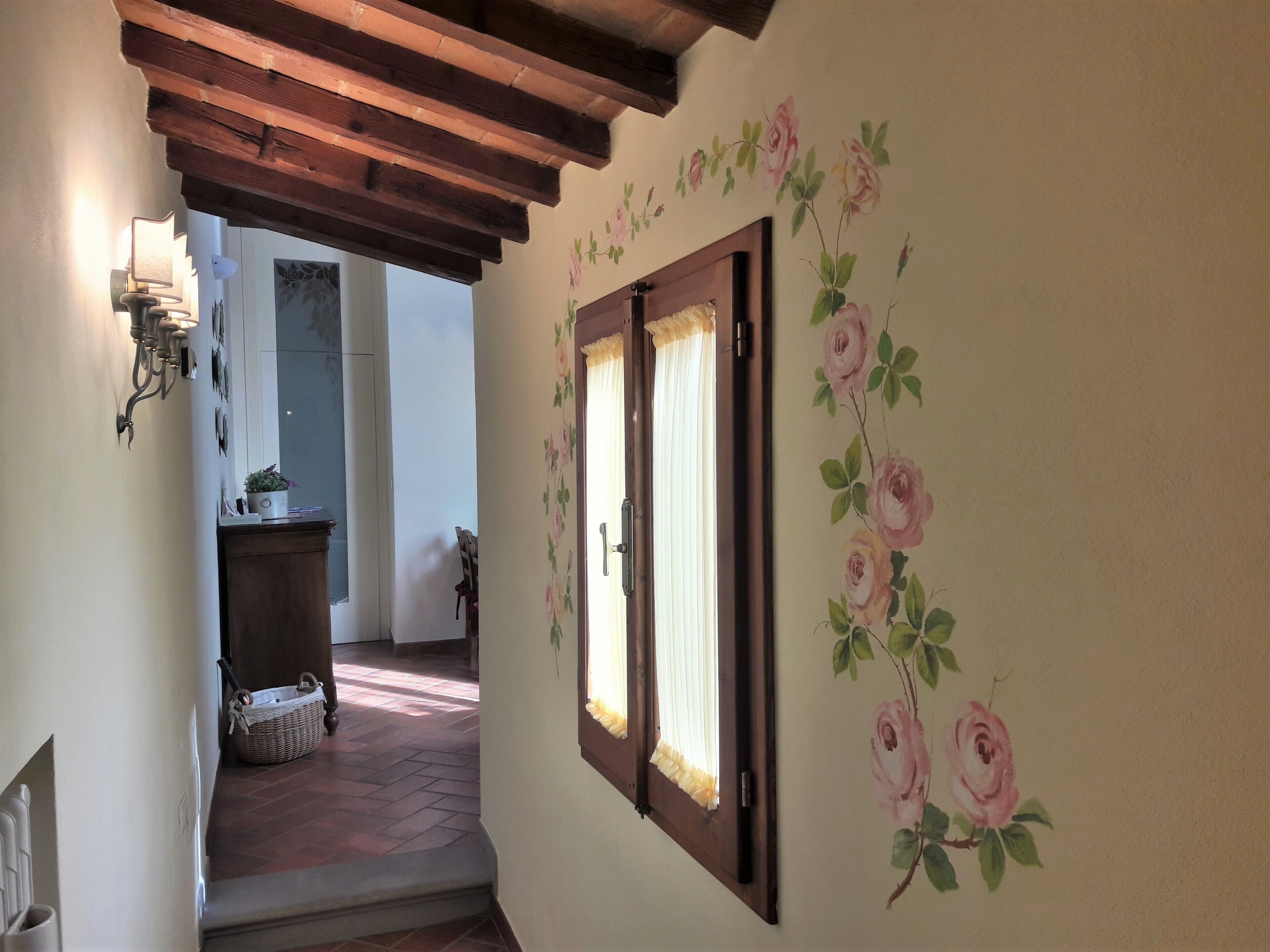 Un pasillo con techo de madera, una ventana con papel tapiz floral y una cesta de mimbre en el suelo.