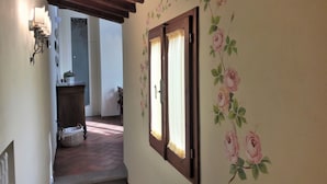 A hallway with a wooden ceiling, a window with floral wallpaper, and a wicker basket on the floor.