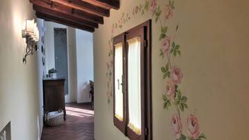 Un pasillo con techo de madera, una ventana con papel tapiz floral y una cesta de mimbre en el suelo.