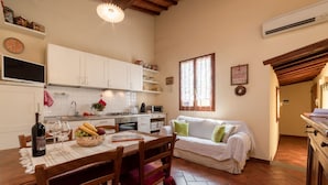 A cozy kitchen with white cabinets, a dining table with chairs, a white sofa, and a window with curtains.