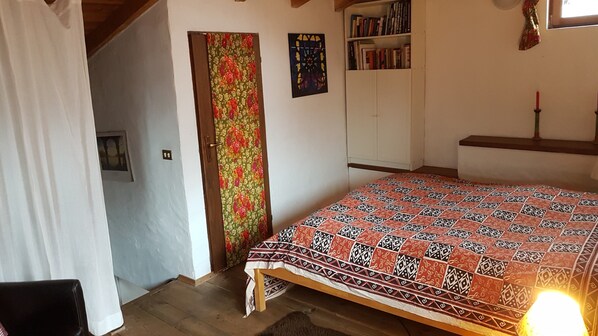 A bedroom with a bed, a wardrobe, a bookshelf, and a door with floral curtains.