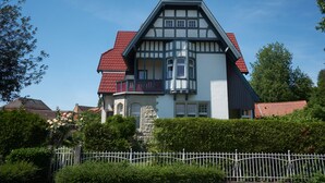 Een groot, twee verdiepingen hoog huis met een steil dak, een stenen fundering en een balkon met rode leuningen.