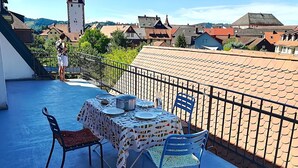 Een balkon met een tafel voor twee, met uitzicht op een stad met traditionele gebouwen en een toren.