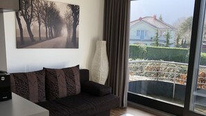 A modern living room with a dark sofa, a white coffee table, and a large window offering a view of a house and trees. - City-Apparte One - Modern apartment building in a central location (Gronau)