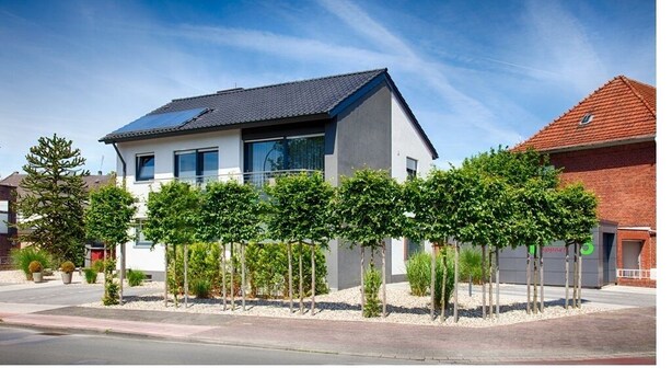 A modern two-story house with a flat roof and solar panels, surrounded by a well-maintained garden with young trees and shrubs. - City-Apparte One - Modern apartment building in a central location (Gronau)